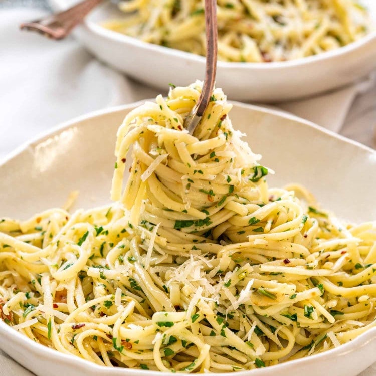 a fork twirling linguini in a plate full of aglio e olio.