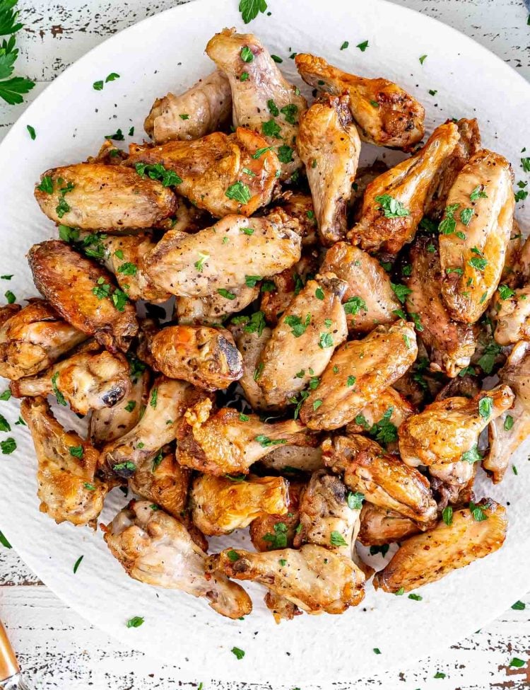 air fryer chicken wings on a round white serving platter garnished with parsley.