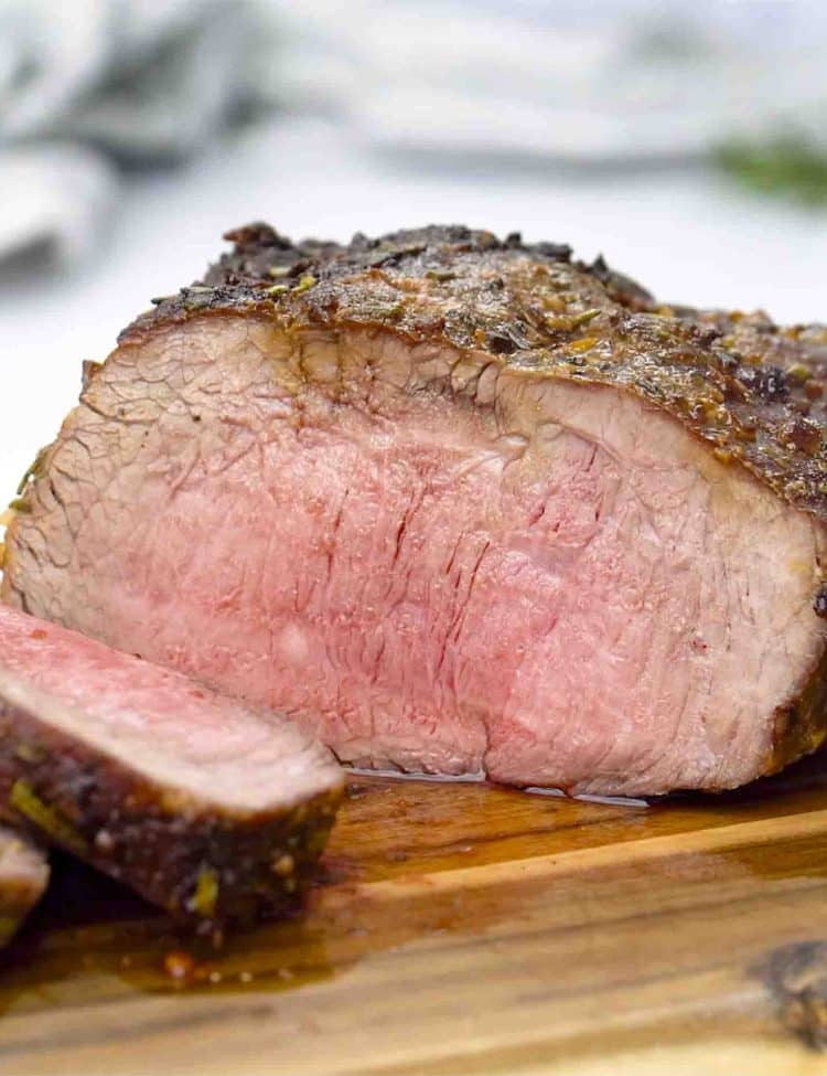 a roast beef made in the air fryer sliced on a cutting board.