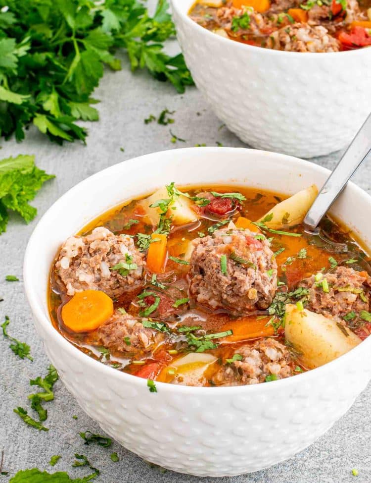 albondigas soup in a white bowl with a spoon inside.