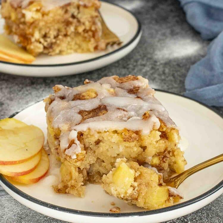 Slice of apple fritter cake on a plate with glaze drizzle and apple slices, showing moist and tender crumb.