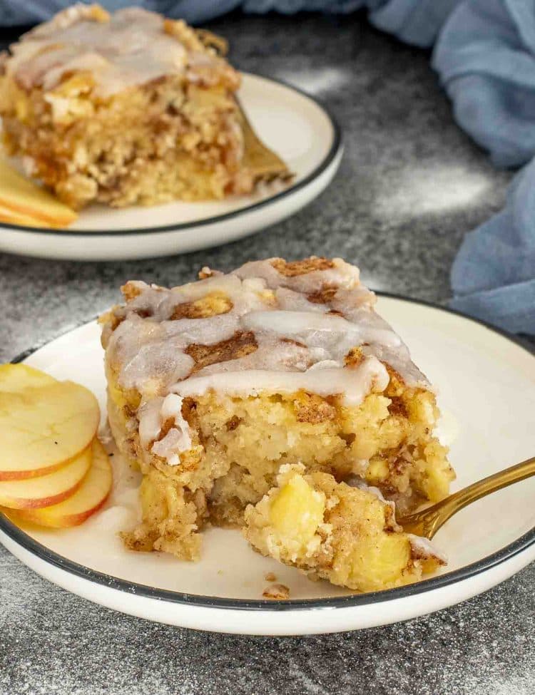 Slice of apple fritter cake on a plate with glaze drizzle and apple slices, showing moist and tender crumb.