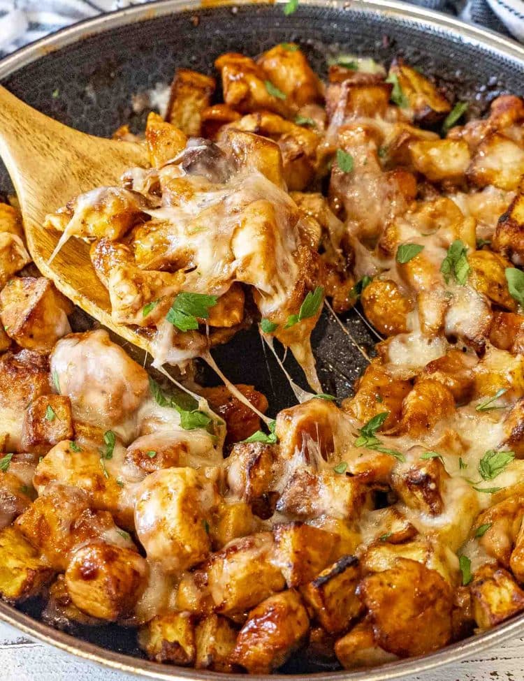 Juicy chunks of chicken and crispy potatoes coated in sticky BBQ sauce with cheese stretching in hot skillet.