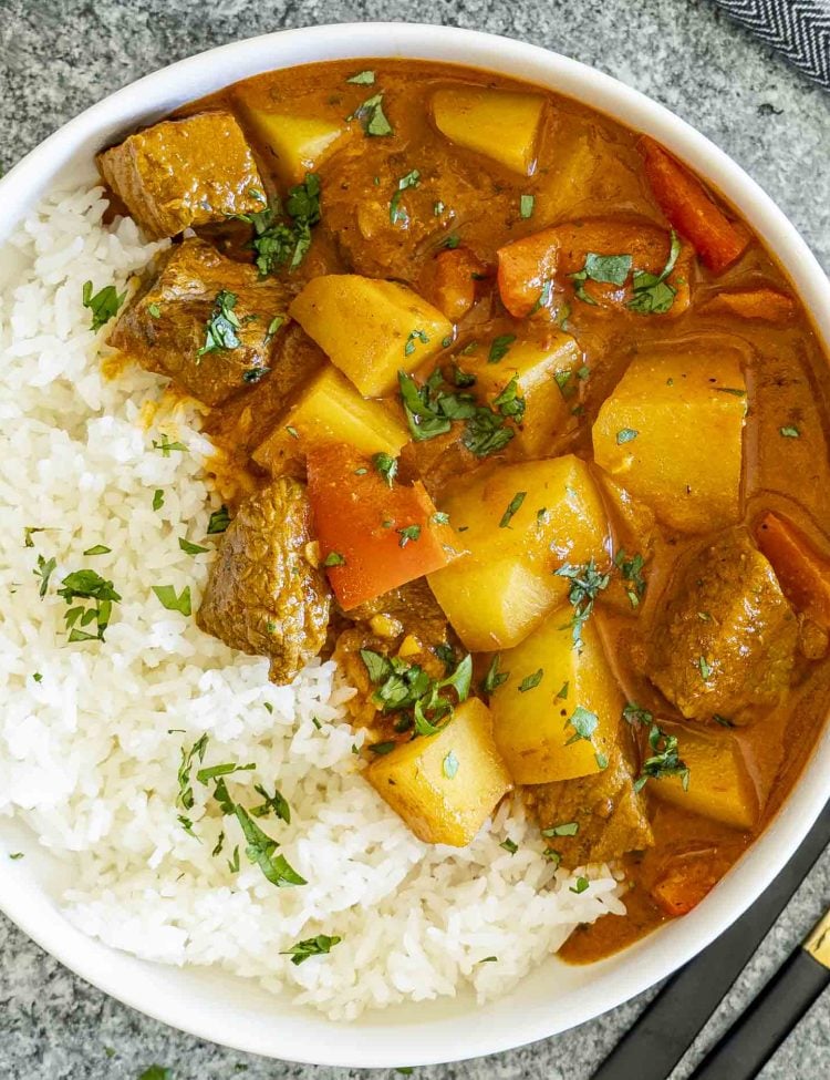 Overhead view of beef and potato curry served with rice in a white bowl, garnished with fresh chopped cilantro.