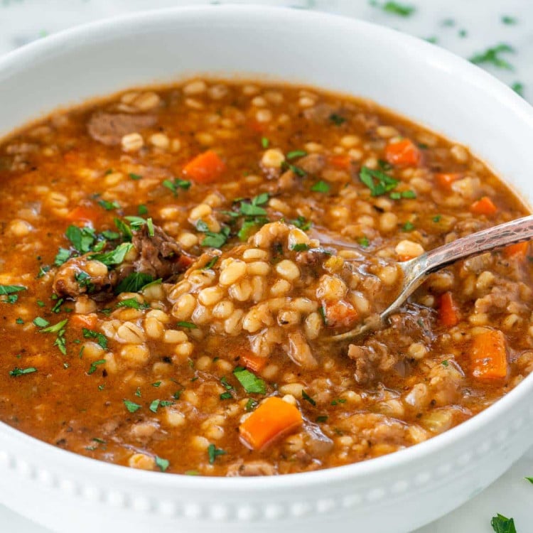 beef barley soup in a white bowl with a spoon inside.