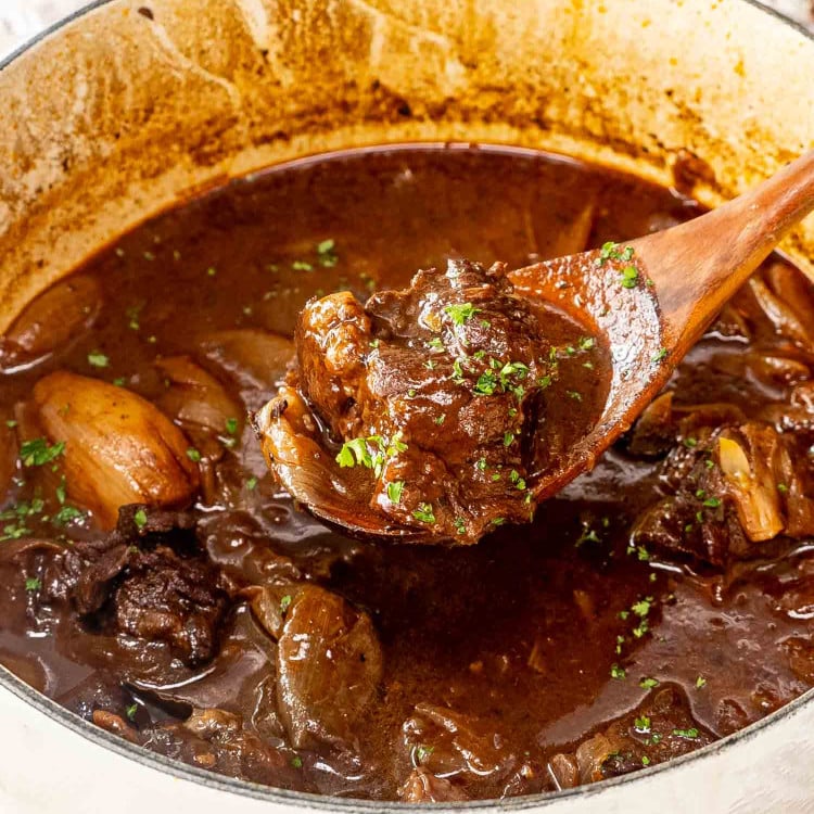 beef stifado (greek beef stew in a dutch oven with a wooden spoon inside.