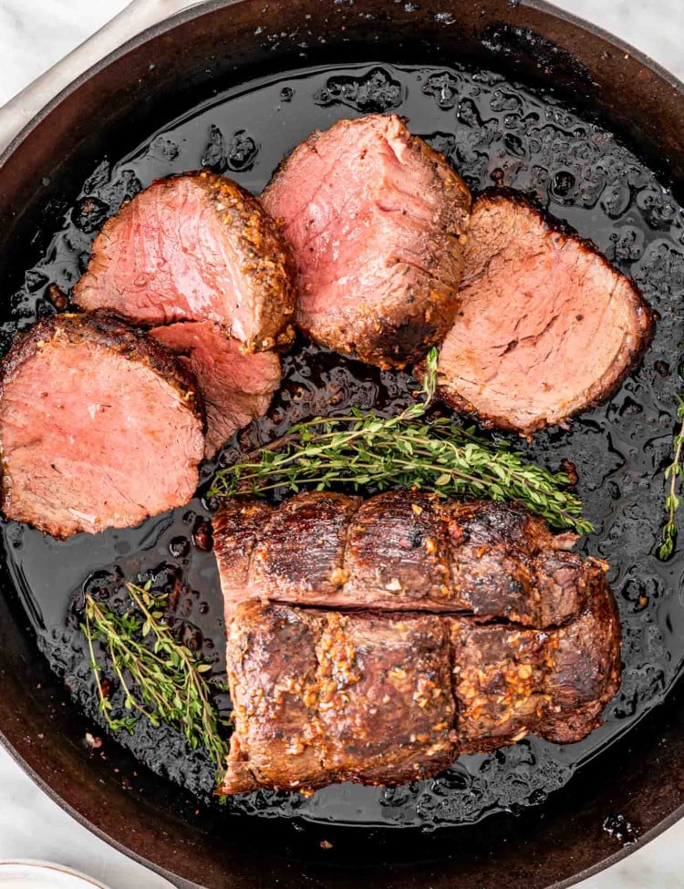 a beef tenderloin with half of it cut in slices in a cast iron skillet.