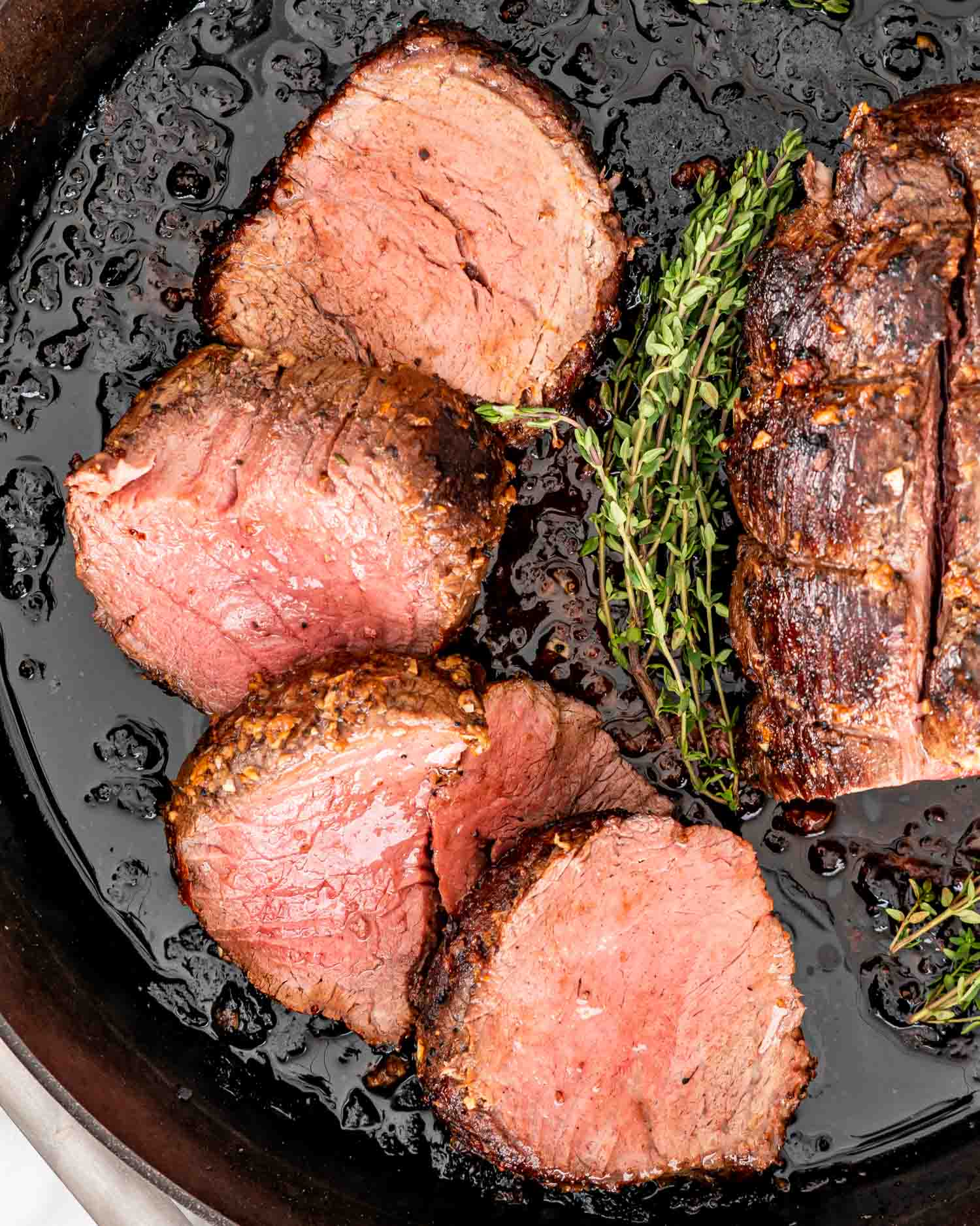a beef tenderloin with half of it cut in slices in a cast iron skillet.