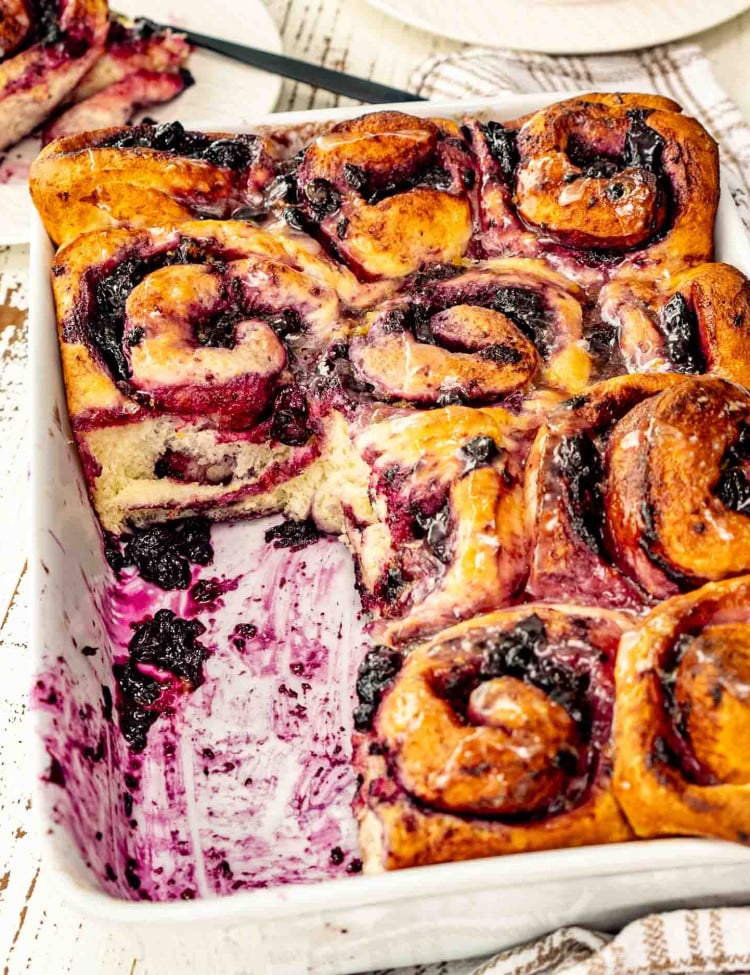 fresh blueberry rolls in a white baking dish with a lemon glaze on top.