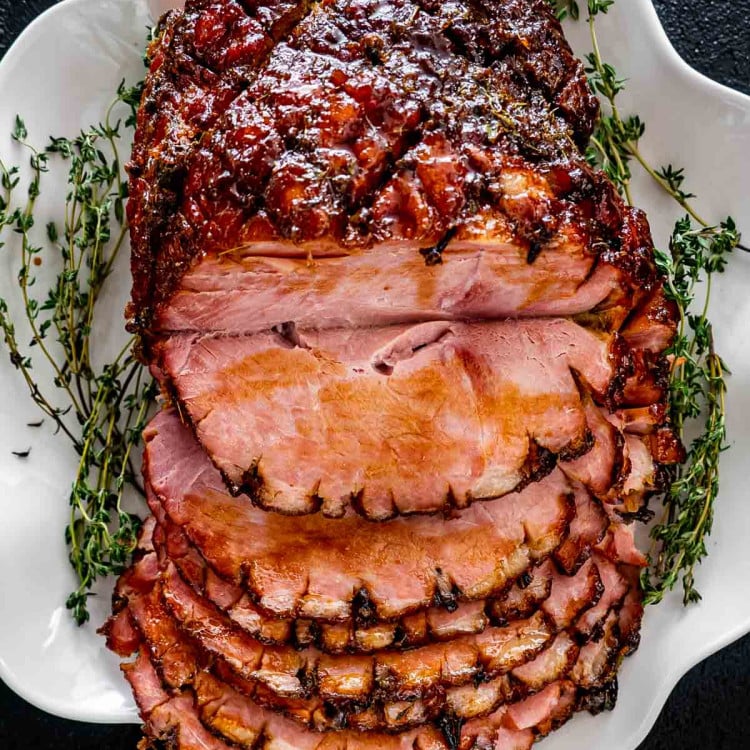 bourbon glazed ham on a white platter sliced garnished with fresh thyme.