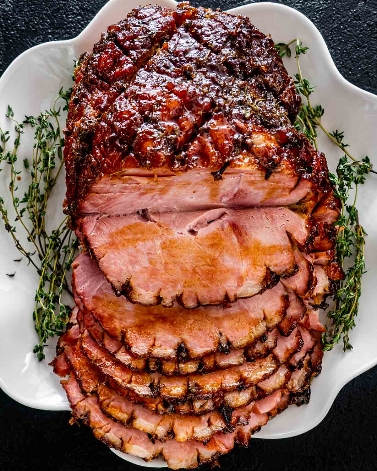 bourbon glazed ham on a white platter sliced garnished with fresh thyme.