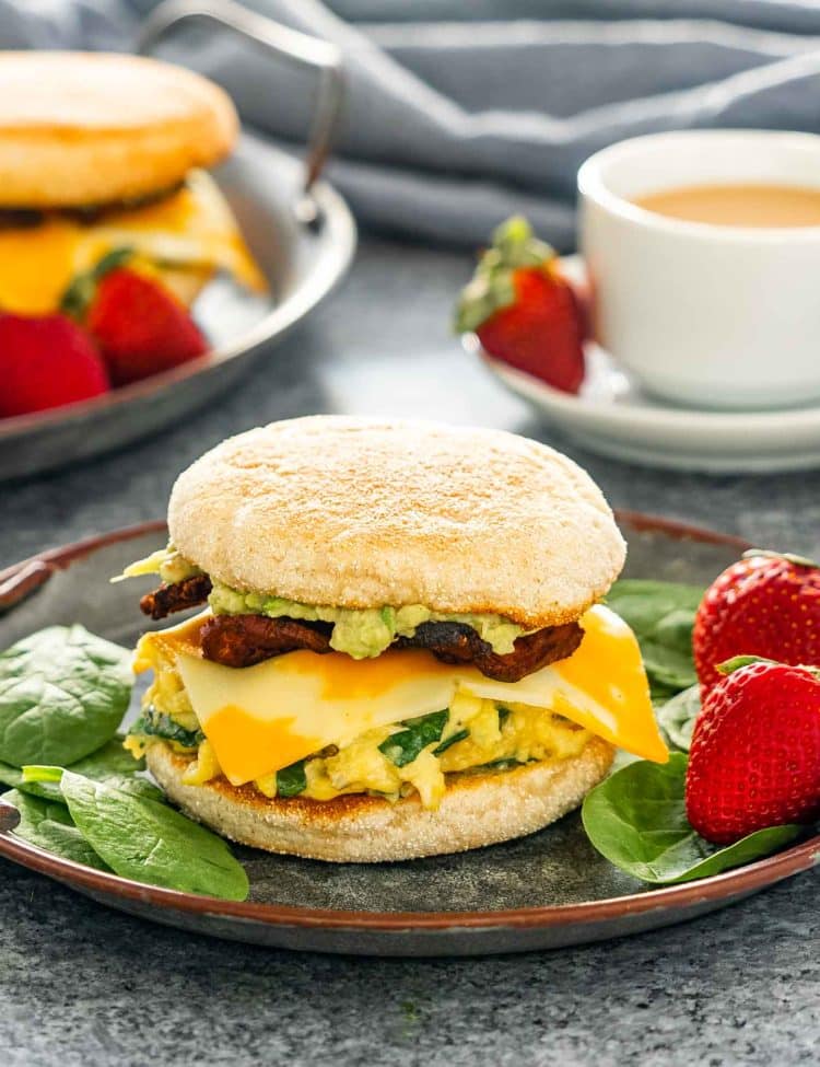 a breakfast sandwich on a metal plate with strawberries on the side.