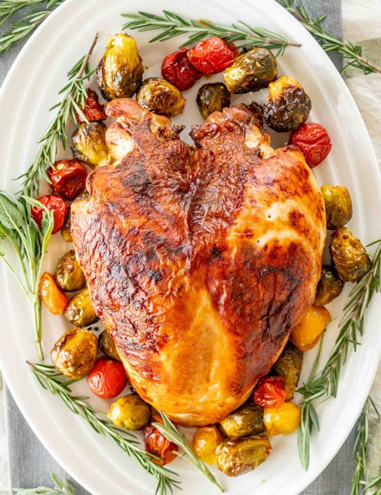 a brined roast turkey breast on a turkey platter garnished with veggies and fresh herbs.