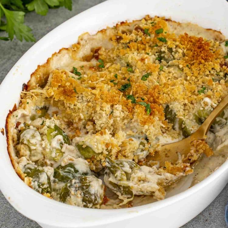 Golden brown Brussels sprouts gratin in a white baking dish with creamy sauce and crispy panko topping, served with gold spoon.