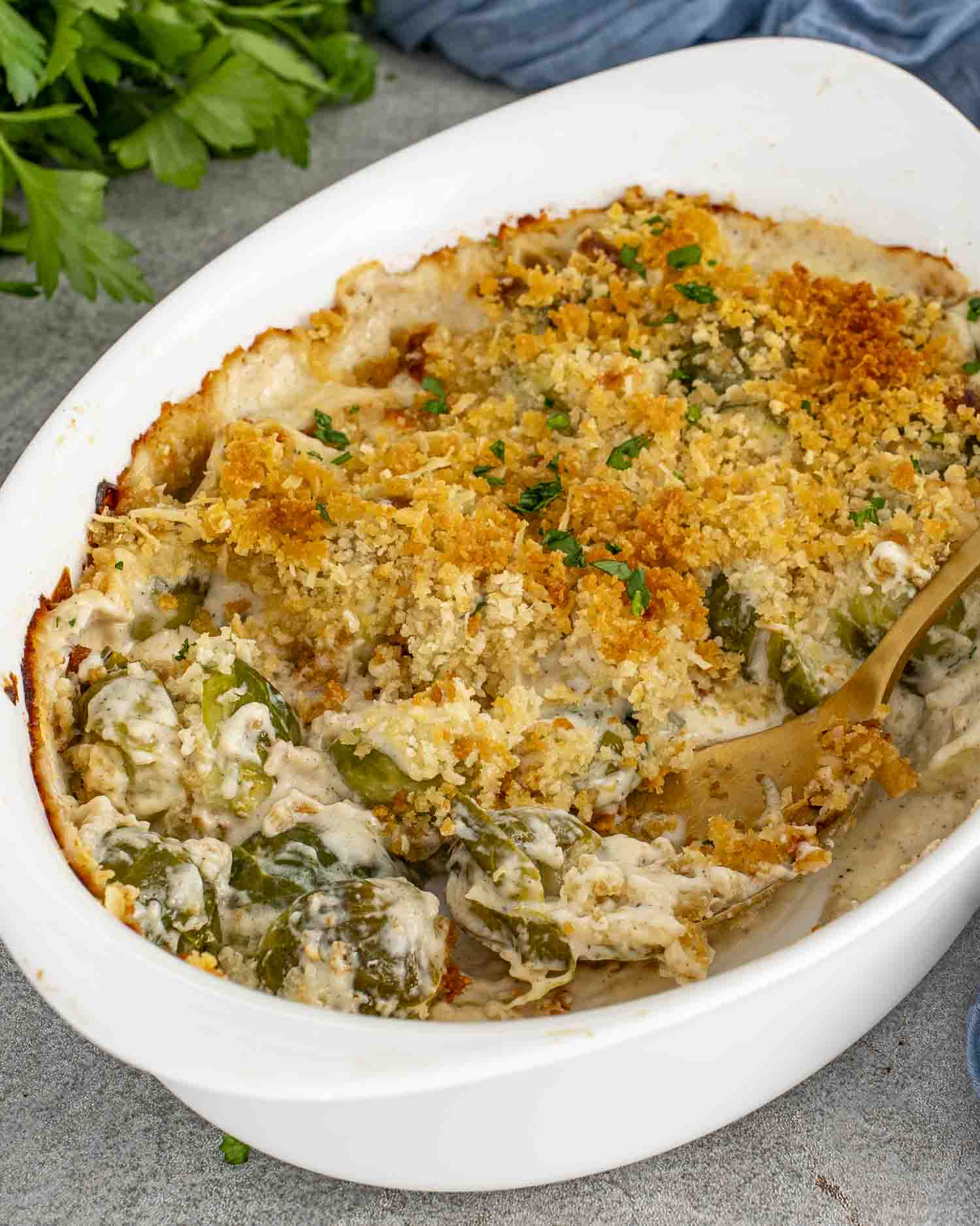 Golden brown Brussels sprouts gratin in a white baking dish with creamy sauce and crispy panko topping, served with gold spoon.