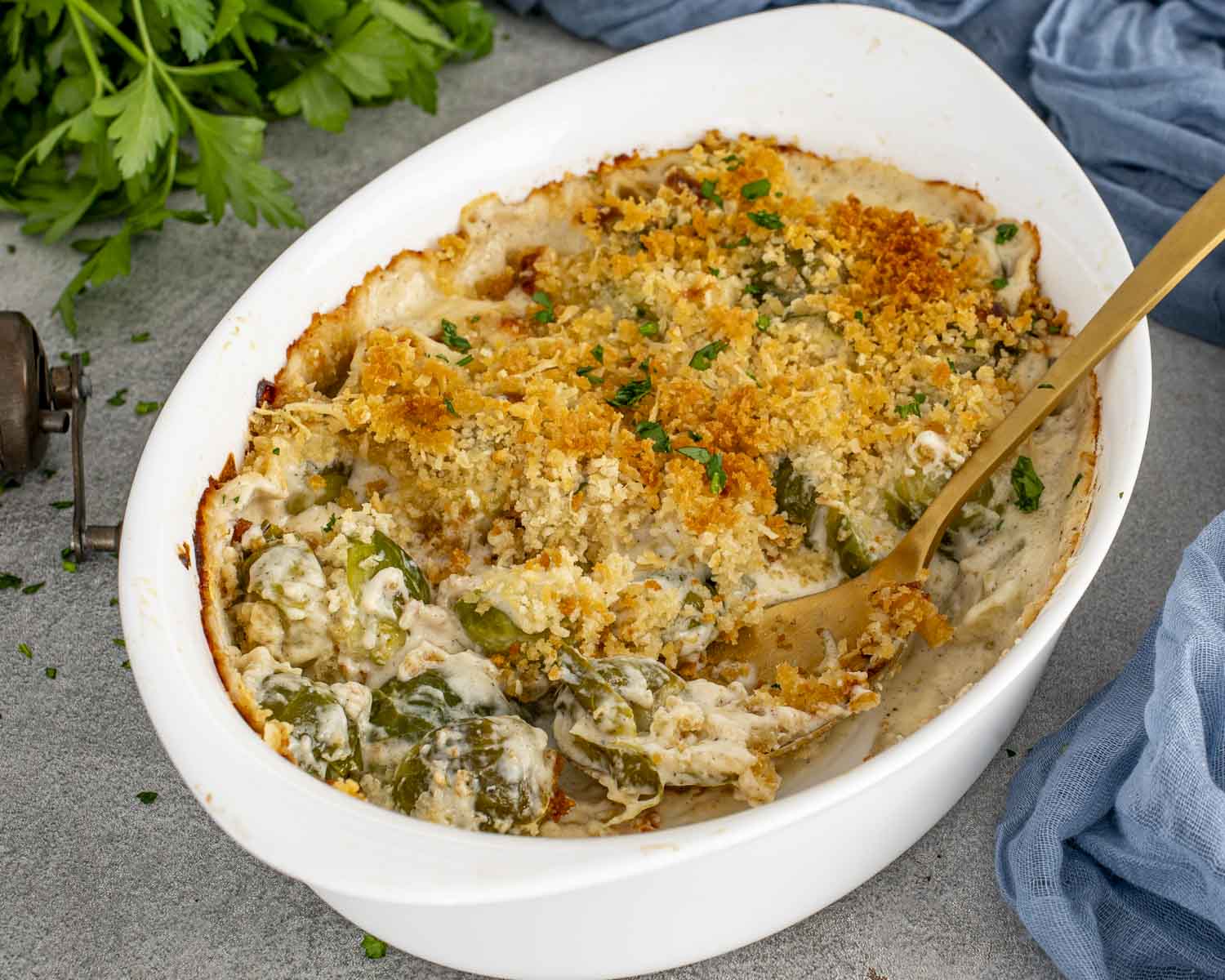 Creamy Brussels sprouts gratin in a white casserole dish with browned breadcrumb crust, melted cheese, and serving spoon ready to scoop.