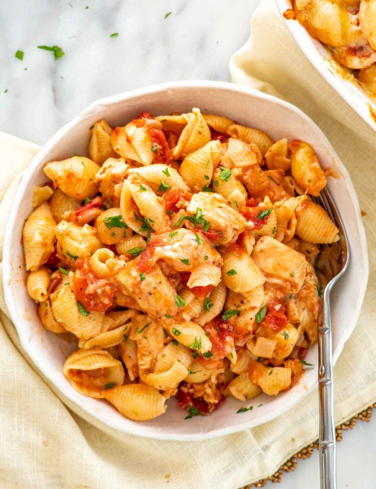 Top view bowl of cheesy chicken casserole featuring tender chicken, pasta shells, tomato sauce, and mozzarella with parsley.