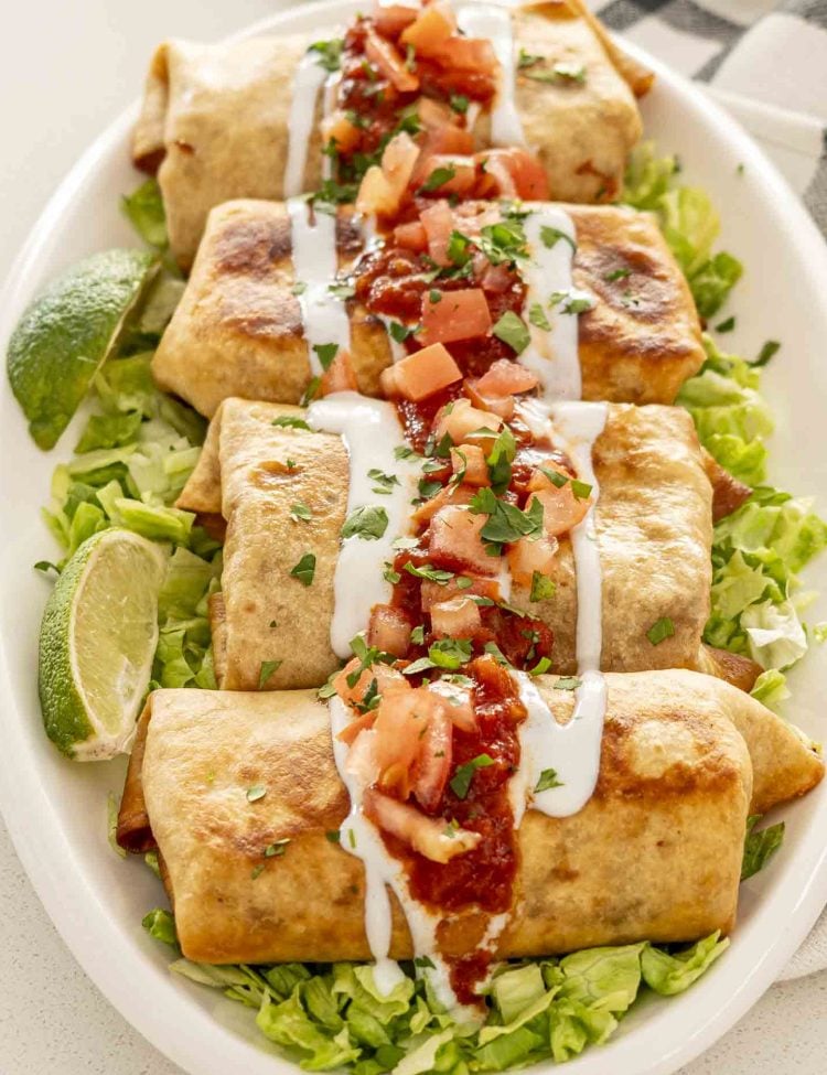 chimichangas on a serving platter on a bed of lettuce garnished with salsa and sour cream.