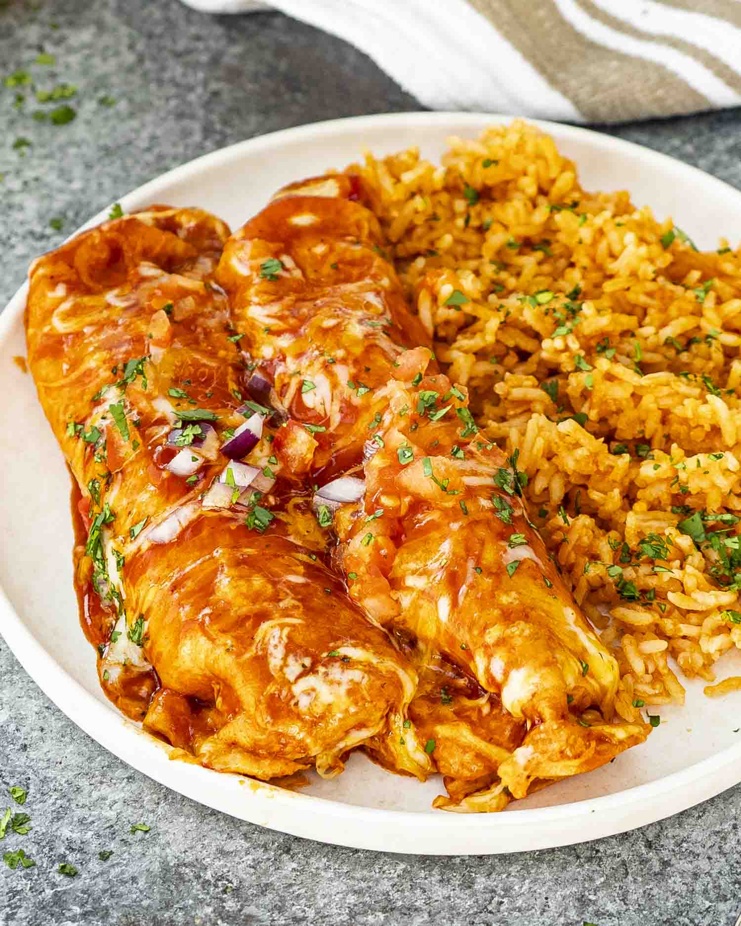 Two saucy chicken enchiladas plated with Mexican rice, garnished with fresh herbs on a white plate.