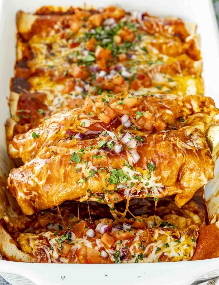A spatula lifting a cheesy chicken enchilada from the dish, revealing the gooey melted interior.