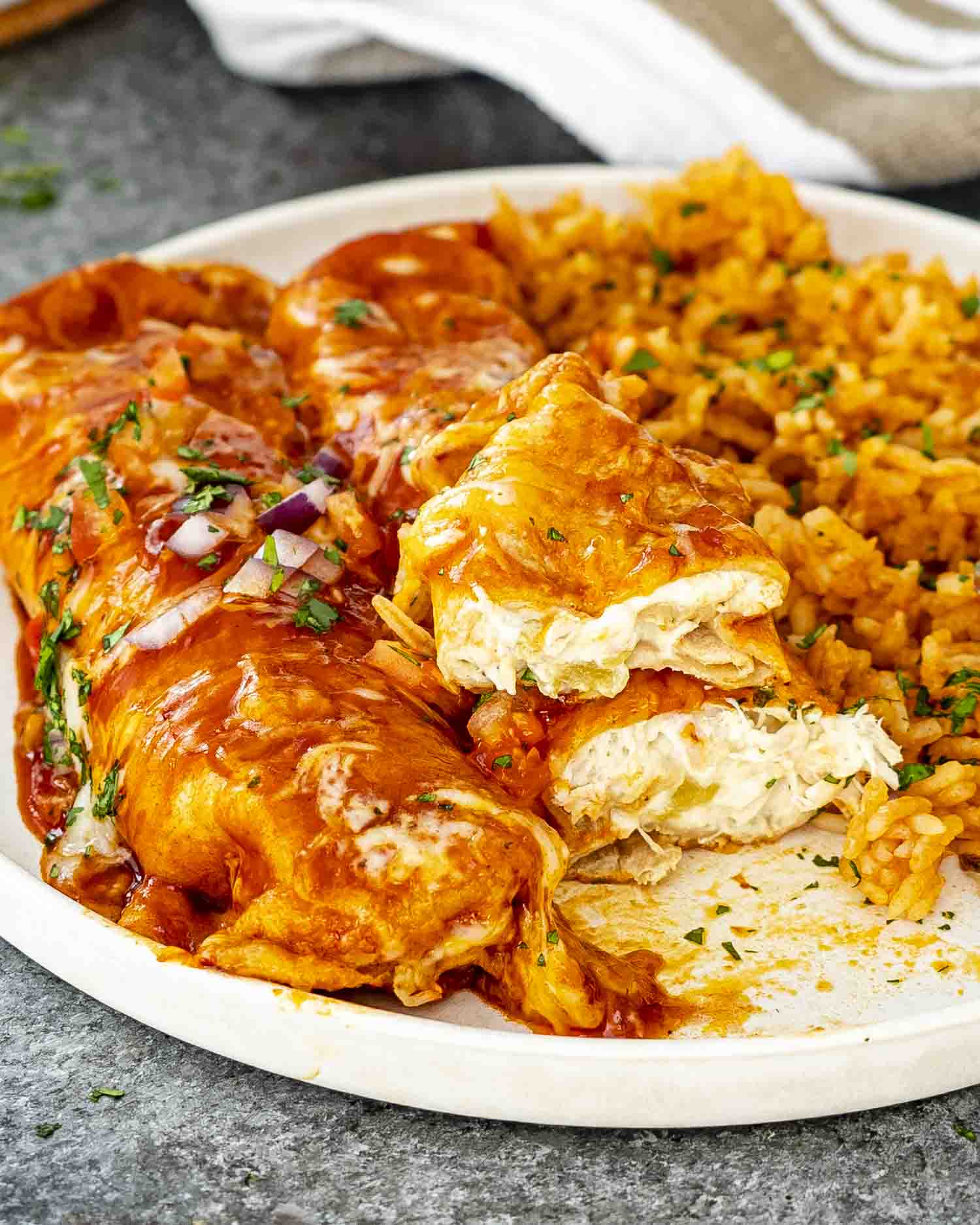 Two saucy chicken enchiladas plated with Mexican rice, garnished with fresh herbs on a white plate.