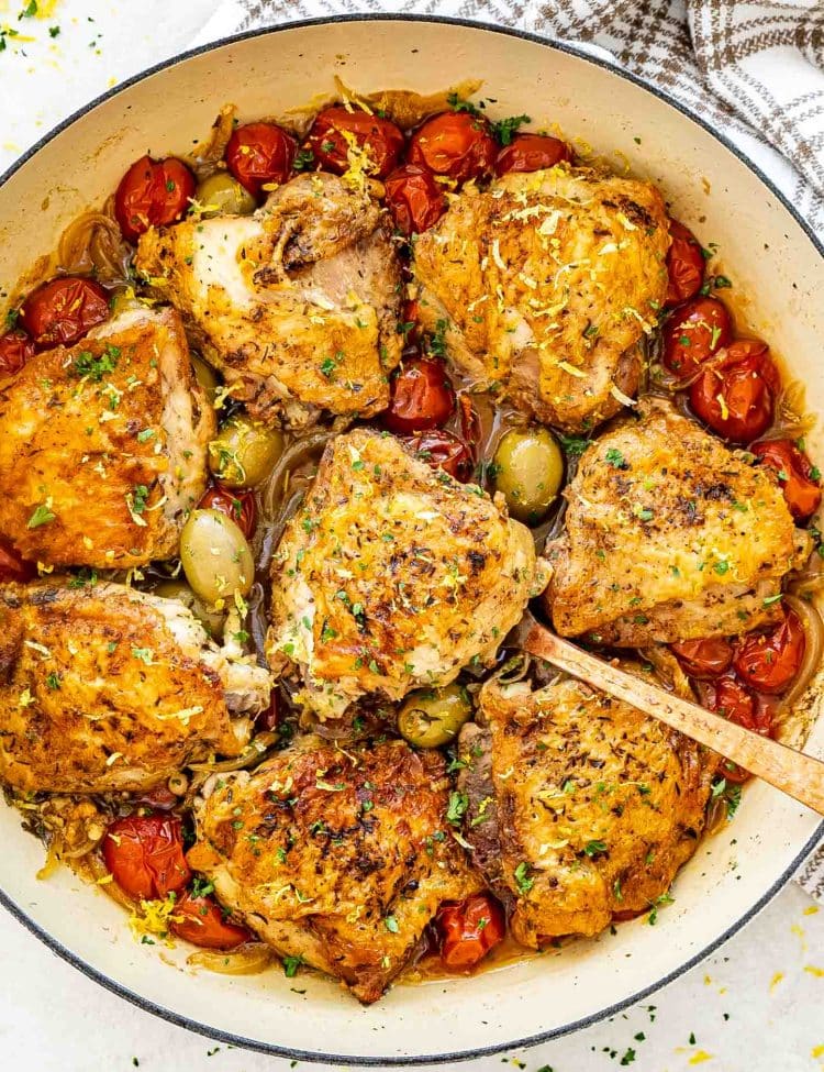 chicken provencal in a dutch oven garnished with parsley and lemon zest.