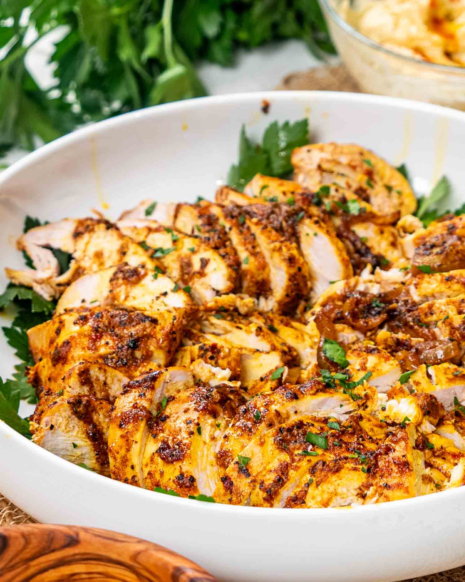 sliced chicken shawarma in a white bowl garnished with parsley and lemon wedges.