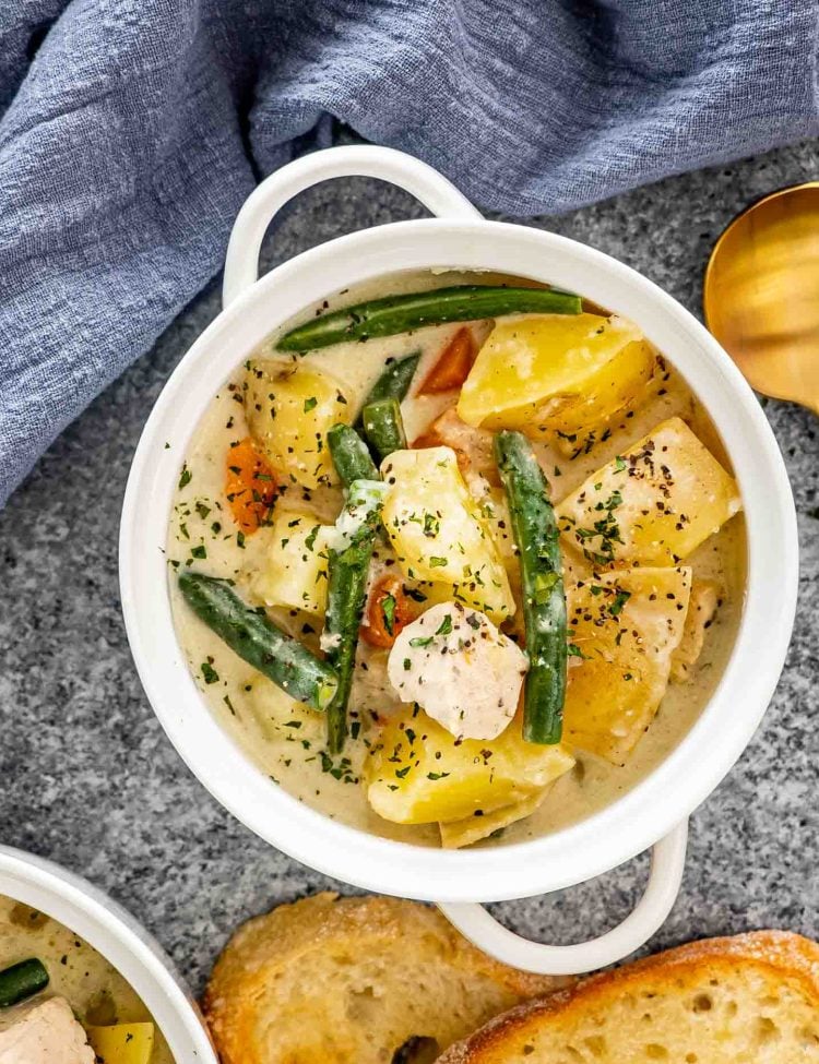 chicken stew in a white bowl next to a couple slices of bread.
