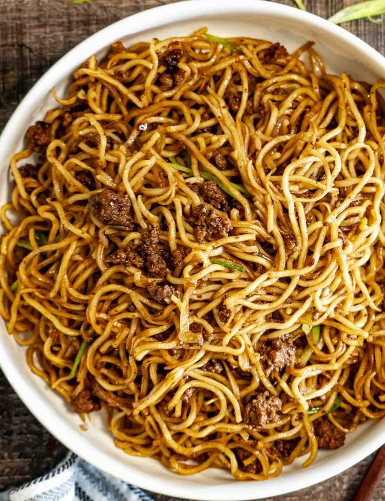 Overhead shot of a large serving bowl filled with glossy Chili Garlic Beef Noodles and sliced green onions.
