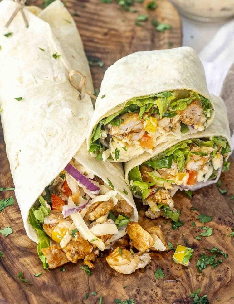 Chipotle Chicken Wraps on a rustic wooden board, cut open to reveal juicy chicken, crisp lettuce, red onion, bell peppers, and melted cheese, garnished with fresh cilantro.