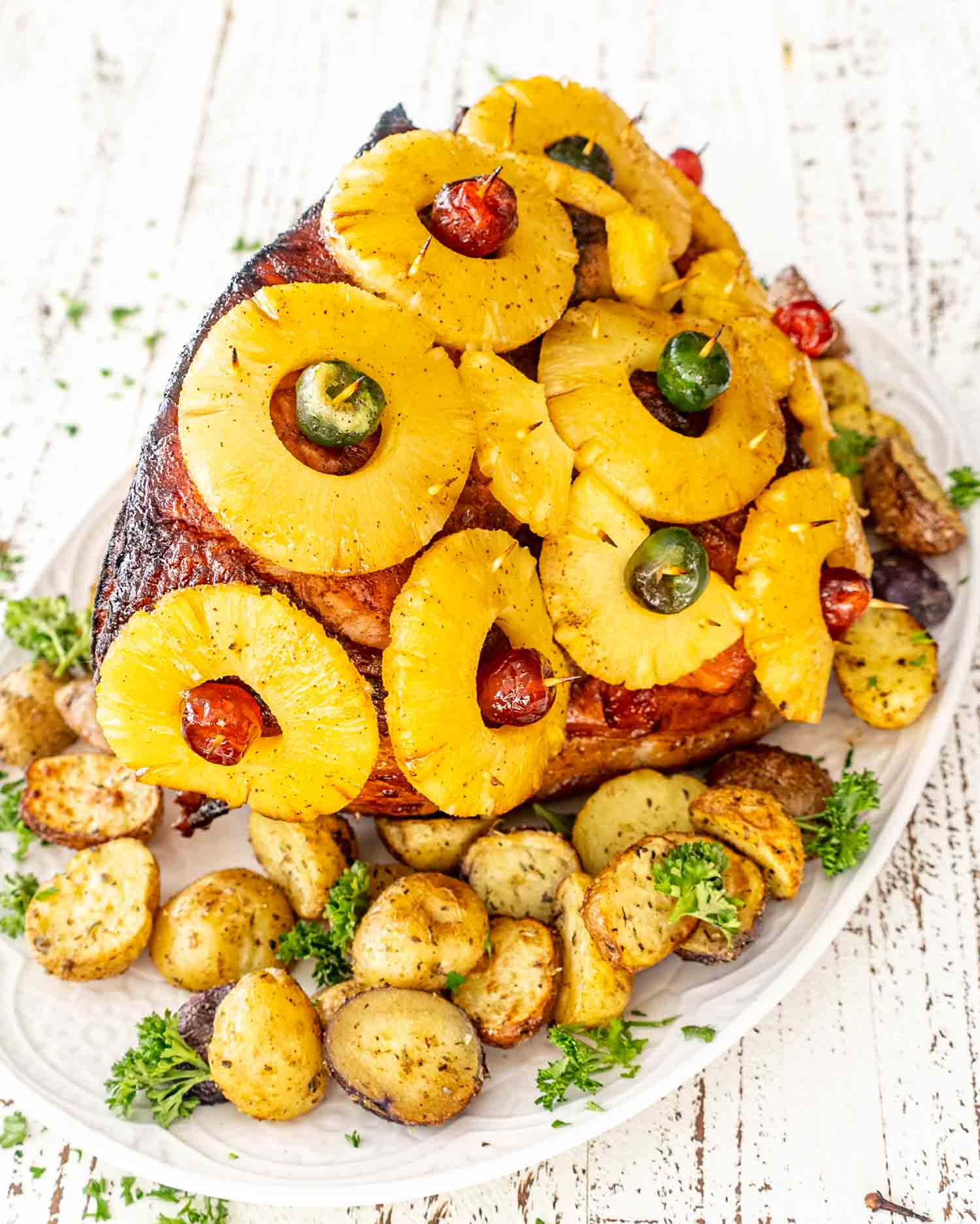 a whole christmas ham fresh out of the oven on a white serving platter.
