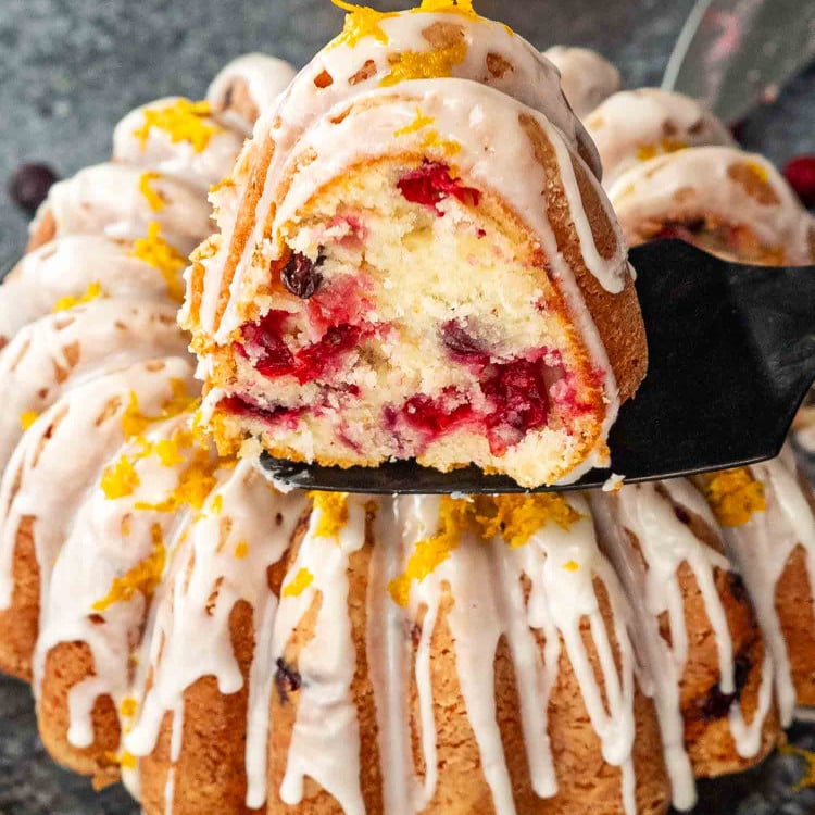 a delicious and gorgeous cranberry coffee cake on a serving plate glazed with a lemon glazed and garnished with orange zest.