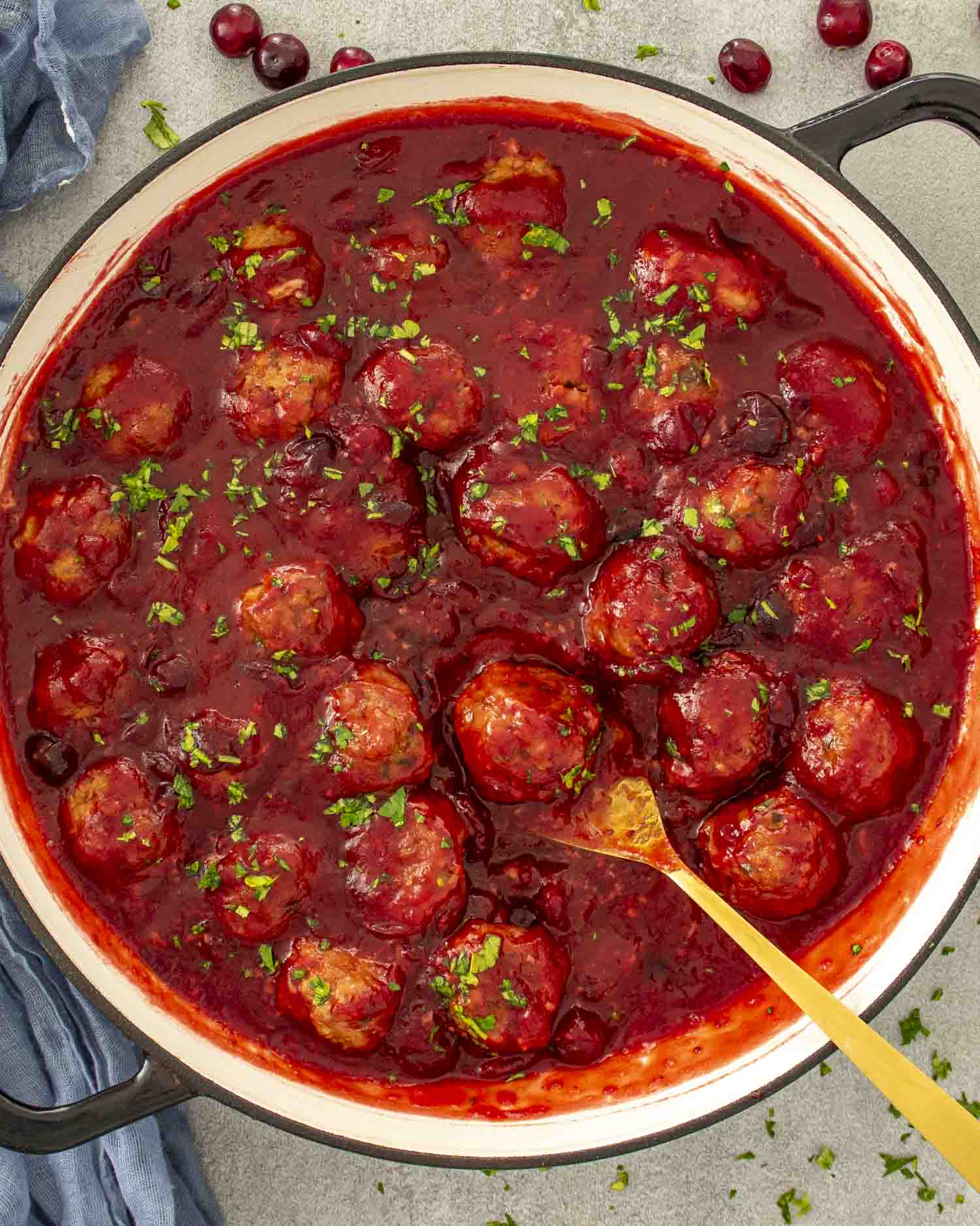 Large skillet filled with cranberry meatballs in rich red cranberry sauce, garnished with parsley and ready to serve.