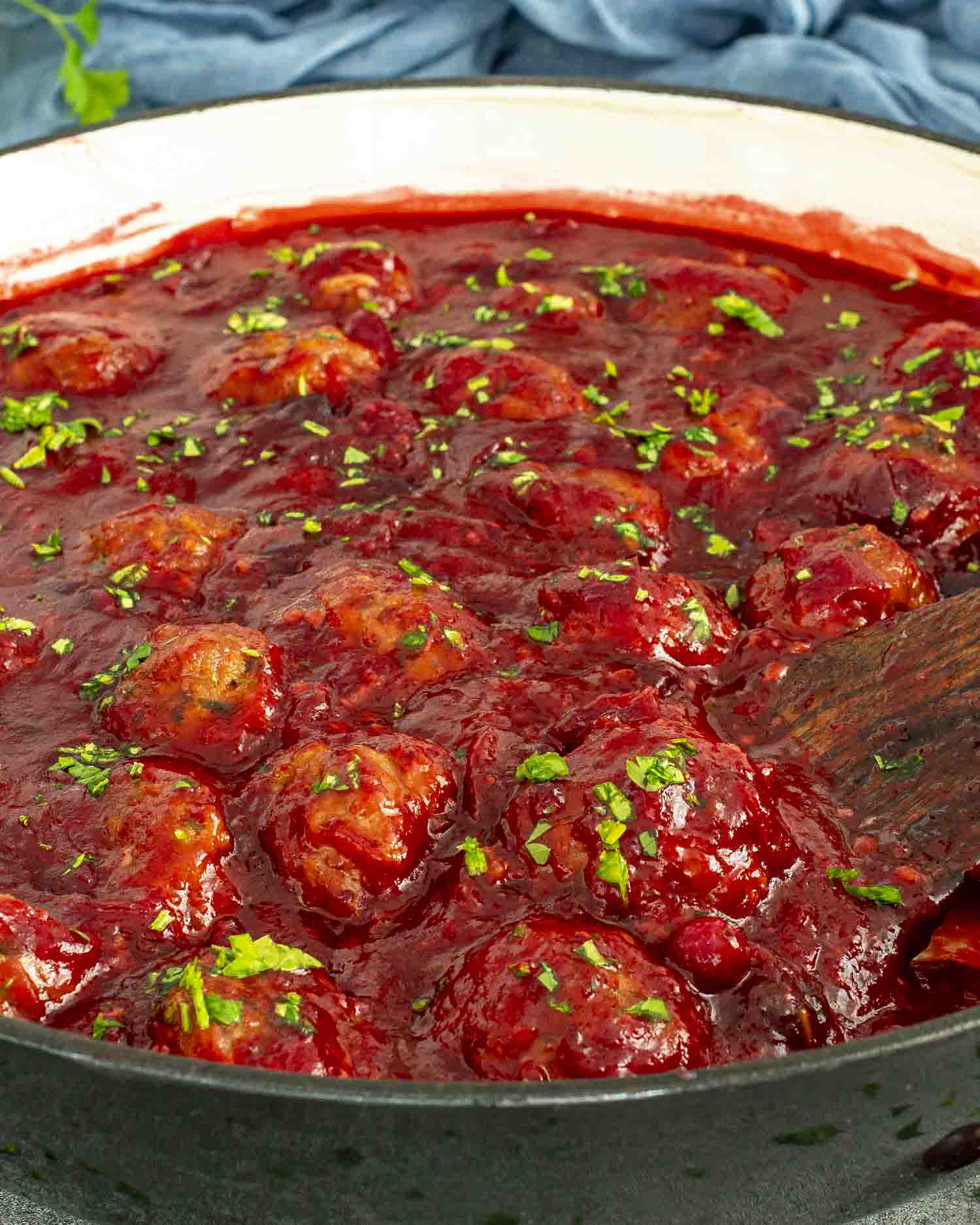 Cranberry meatballs simmering in a skillet with thick, glossy cranberry sauce and sprinkled parsley on top.
