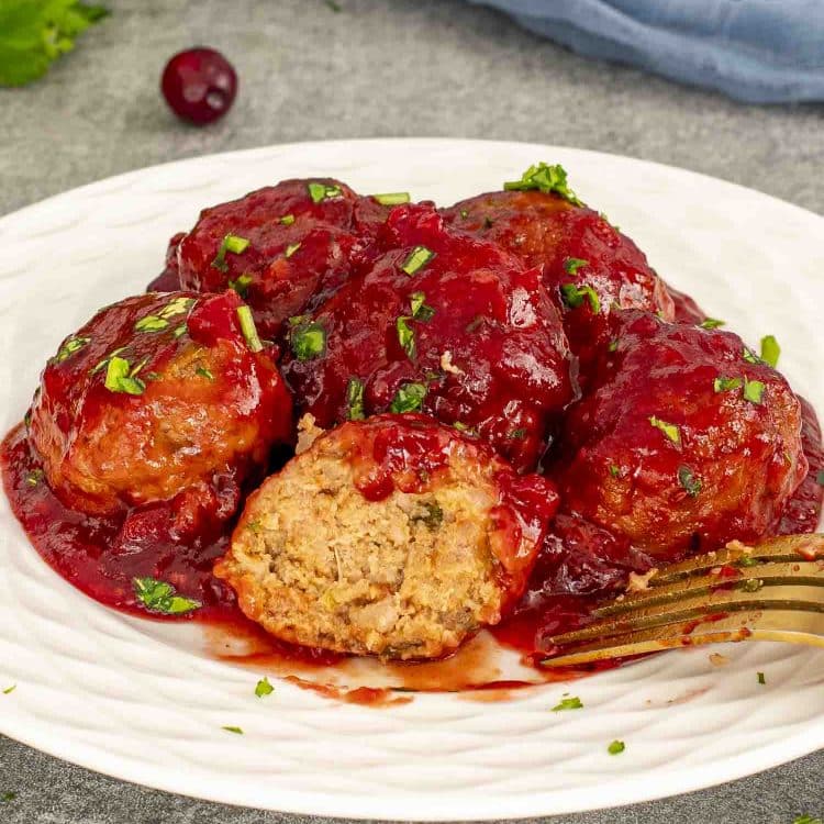 Juicy cranberry meatballs coated in sweet and tangy cranberry sauce on a white plate with fresh parsley garnish.