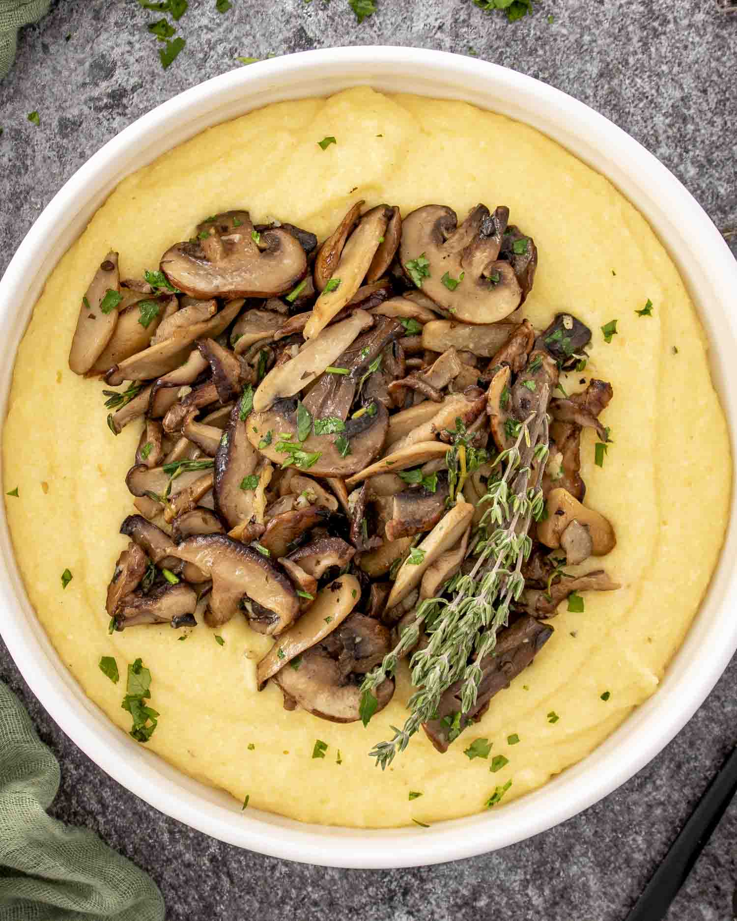 Overhead view of creamy Parmesan polenta with golden mushrooms and fresh thyme garnished with parsley in a round white bowl.