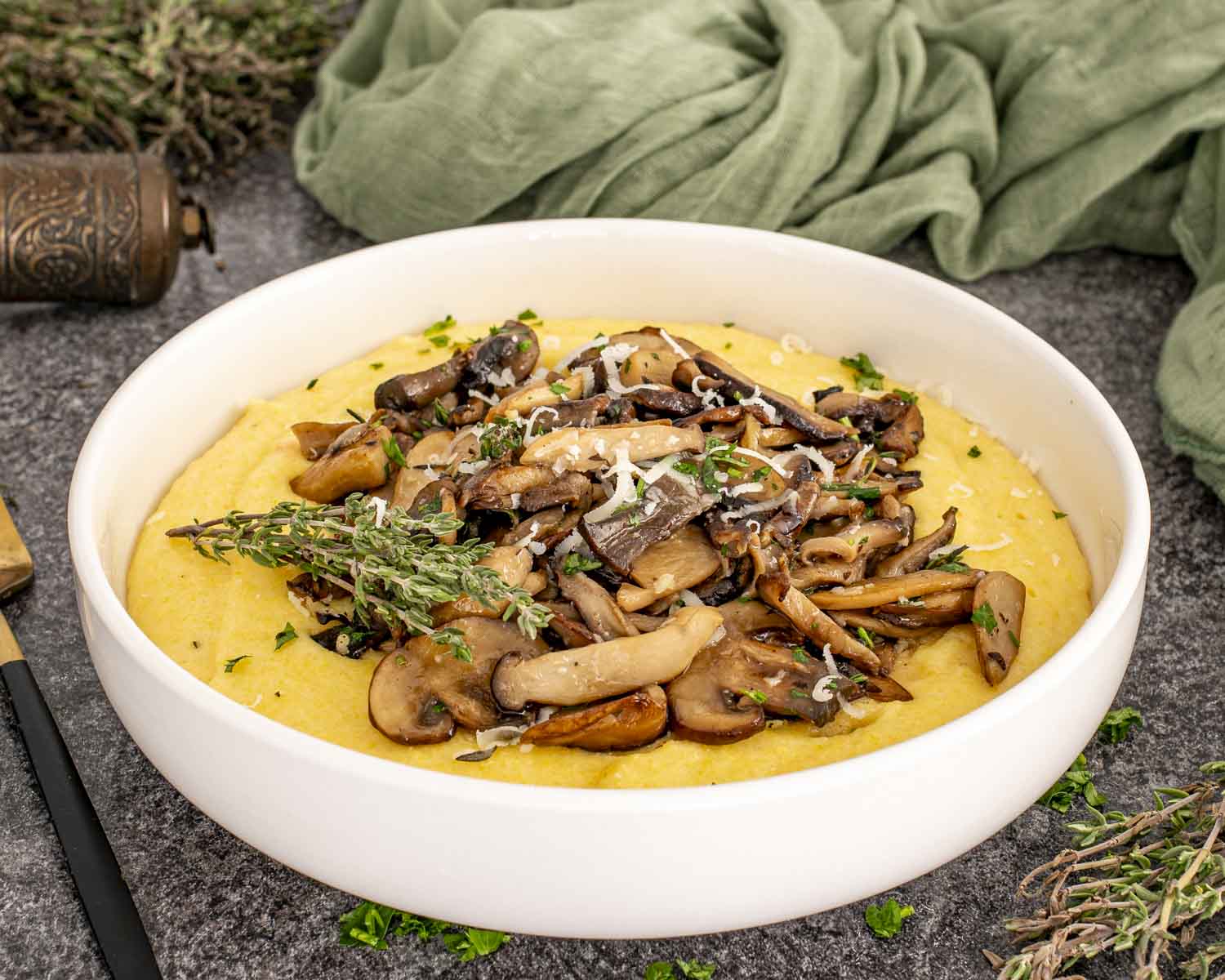 Creamy Parmesan polenta topped with garlic butter mushrooms and herbs in a white bowl, styled with fresh thyme and linen.