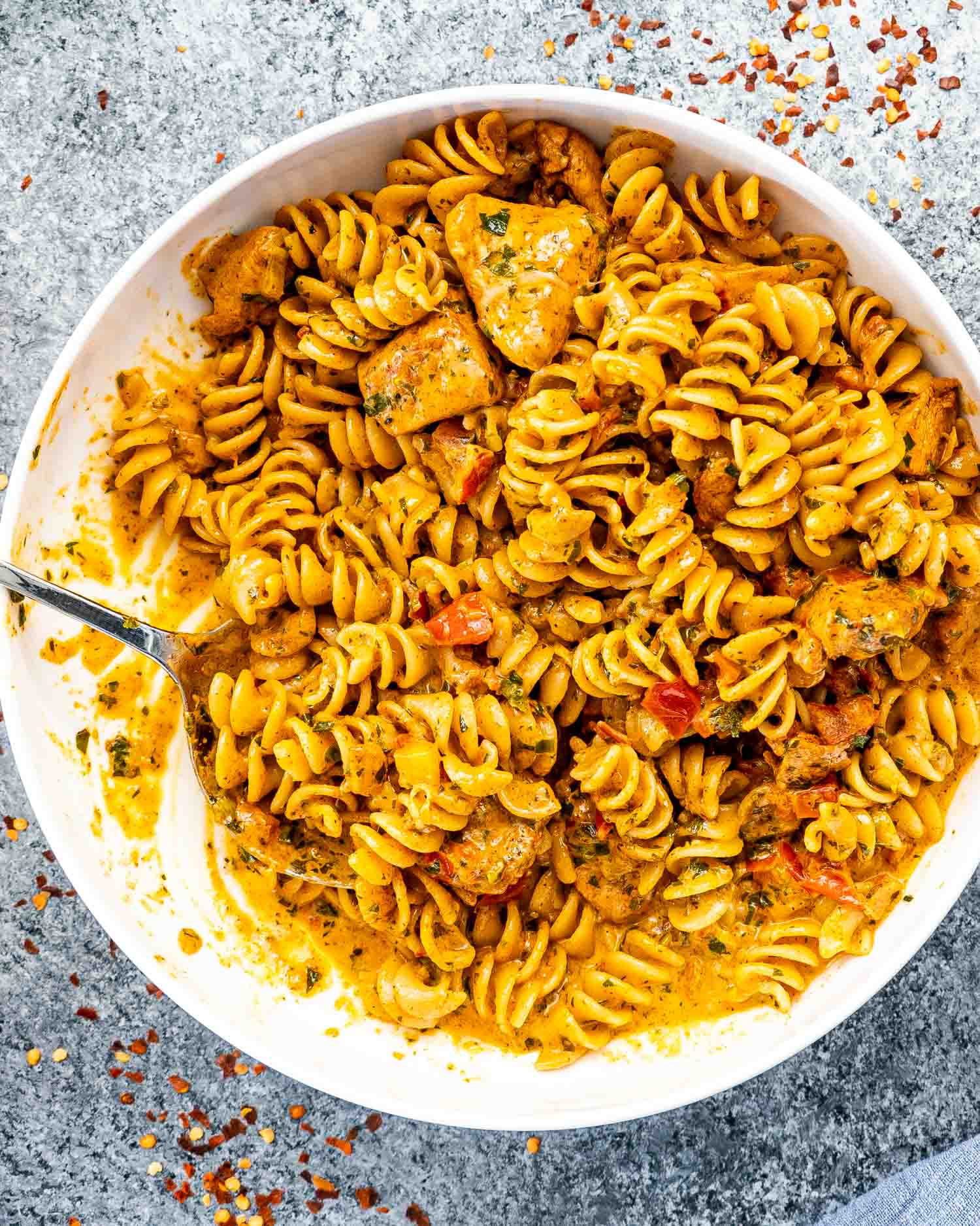 creamy tomato chicken pasta in a white serving bowl with a silver serving spoon.