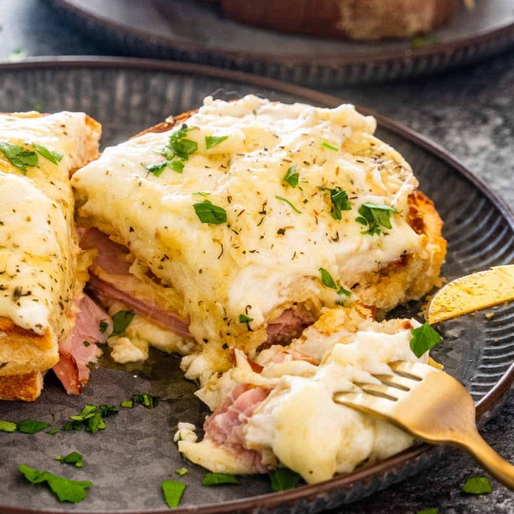 a croque monsieur sandwich on a plate cut in a half with a fork holding a bite.
