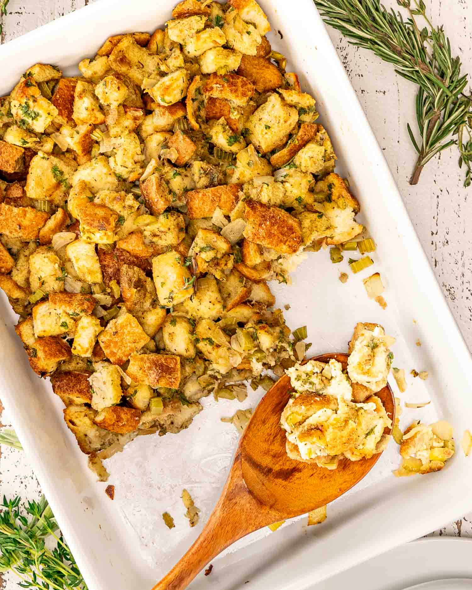 freshly baked bread stuffing in a white casserole dish with a wooden spoon inside.