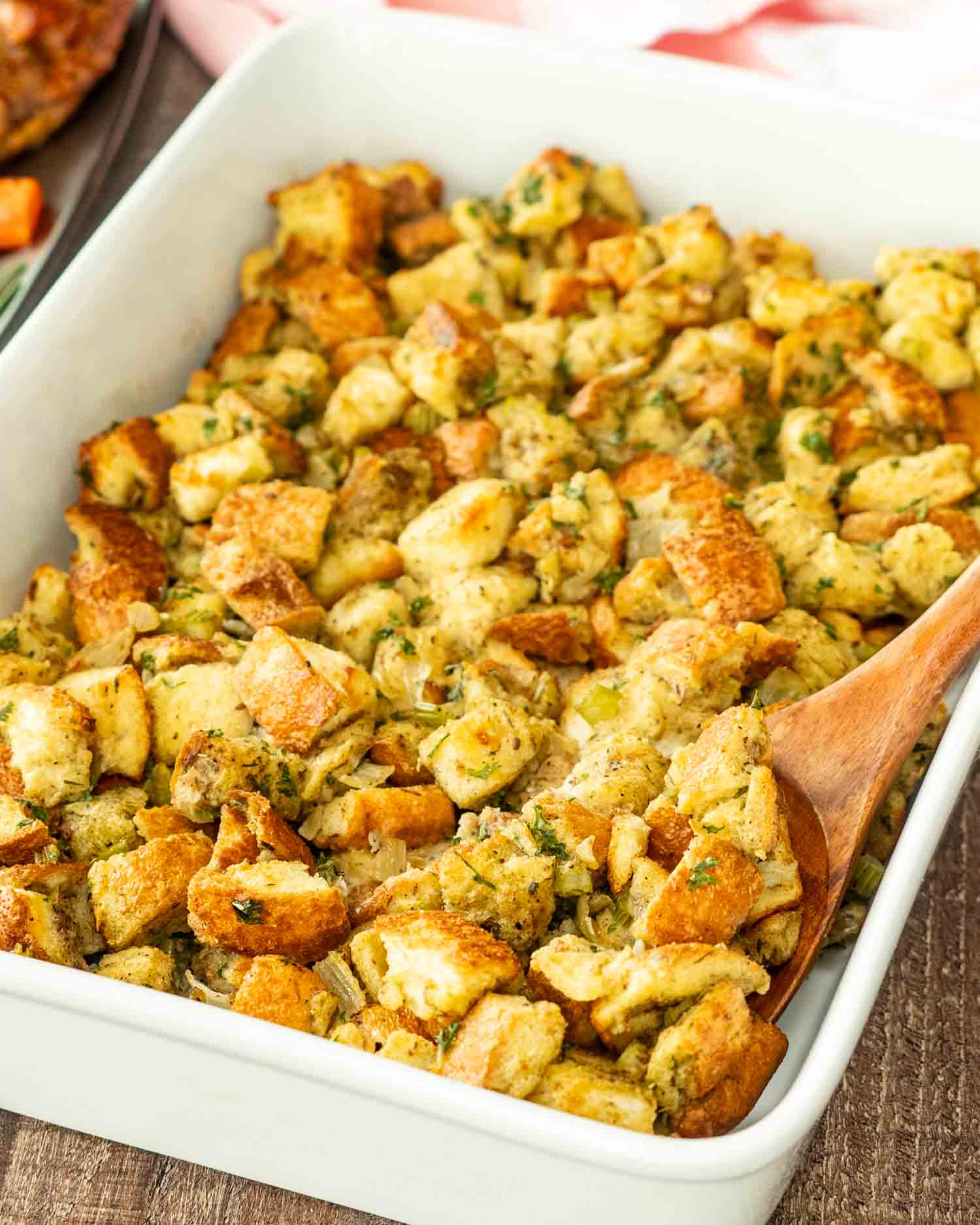 freshly baked bread stuffing in a white casserole dish with a wooden spoon inside.