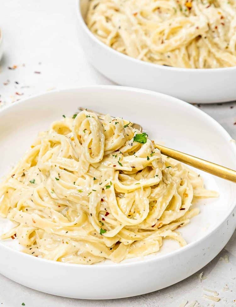 a serving of fettuccine alfredo in a white bowl with a golden fork.