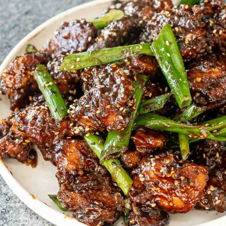 freshly made general tso's chicken garnished with green onions and sesame seeds in a white plate.