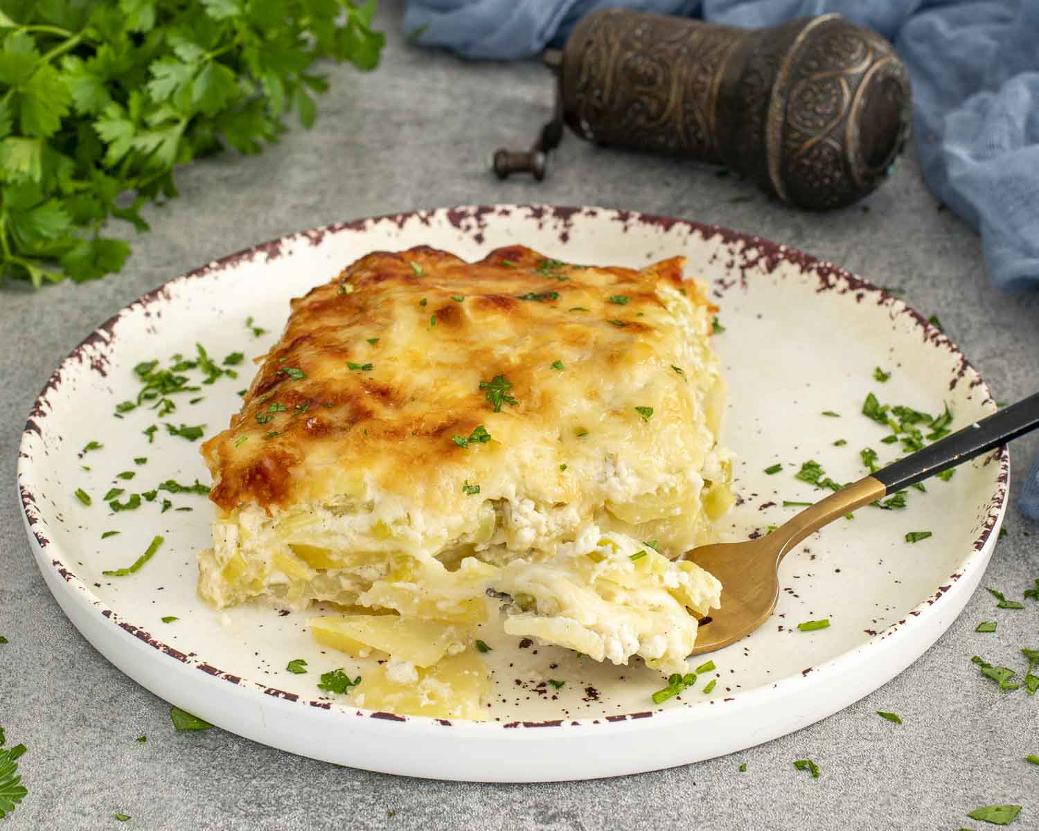 Tender layered scalloped potatoes with leeks, covered in bubbling Gruyère cheese, served on speckled plate with parsley garnish.