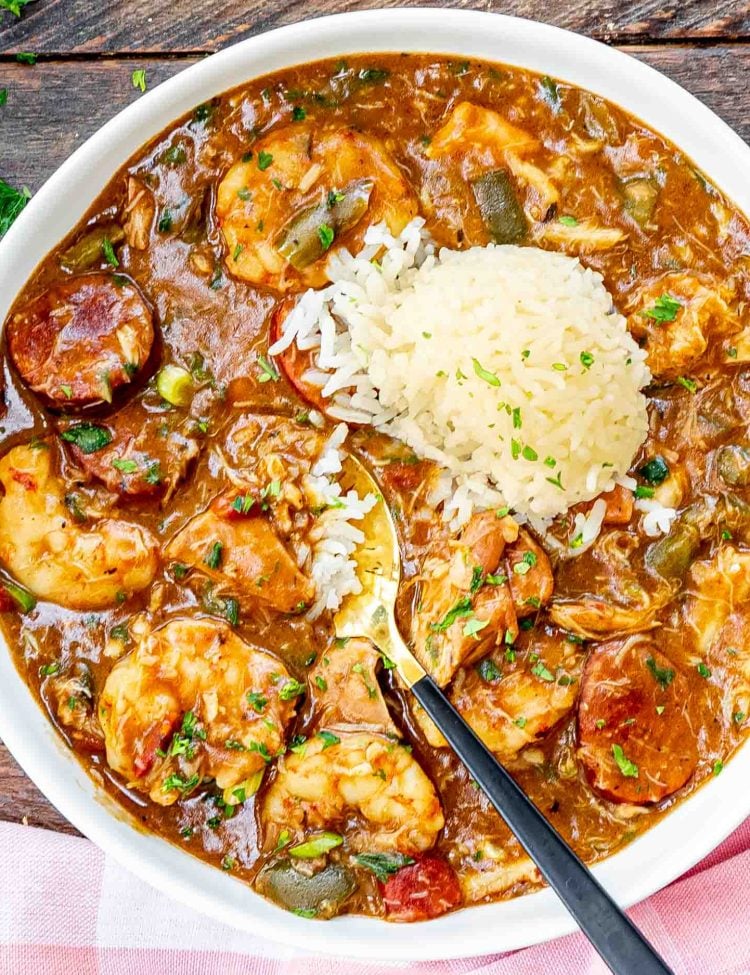 freshly made gumbo in a white bowl with a scoop of rice and garnished with some parsley.