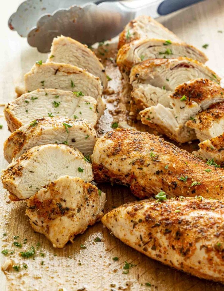 Golden Instant Pot chicken breast sliced on a wooden cutting board with serving tongs, juicy texture visible, sprinkled with parsley.