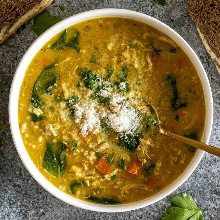 Bowl of Italian Penicillin Soup topped with Parmesan and parsley, served with crusty bread on a dark stone background.