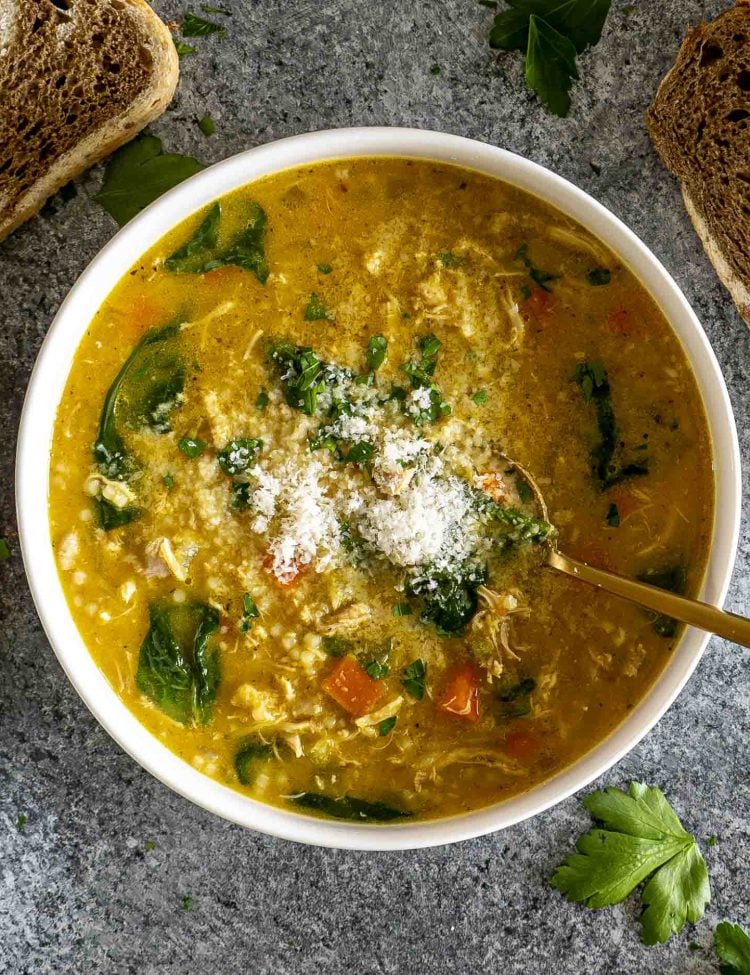 Bowl of Italian Penicillin Soup topped with Parmesan and parsley, served with crusty bread on a dark stone background.