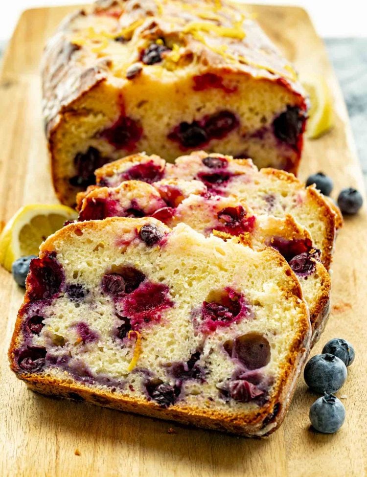 Lemon blueberry loaf sliced on a wooden board, bursting with vibrant blueberries and golden edges, ready to serve.