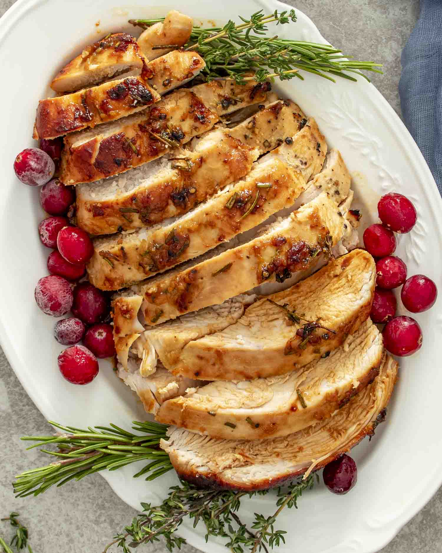 Overhead view of Maple Dijon Glazed Turkey Breast sliced and served with fresh herbs and cranberries on a white plate.